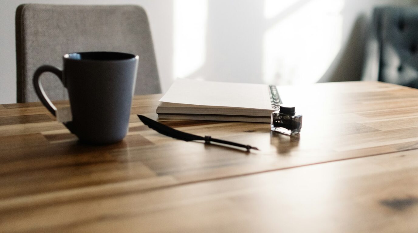Table de travail du concepteur de Ritaaa : carnet ouvert, encre et tasse, lumière du matin.